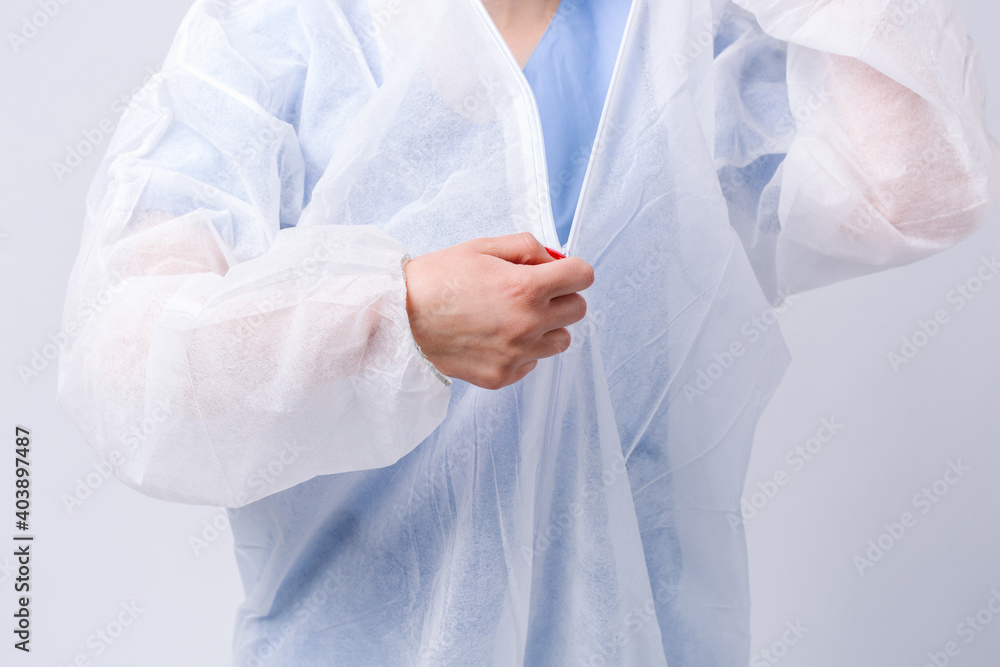 Cropped photo. Doctor removes the protective gown after work shift. Pandemic and coronavirus concept on gray background.