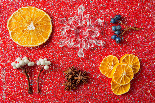 Christmas decorations lying on a red background with sequins. Snowflake, artificial berries, sprig of fir, star anise, etc.