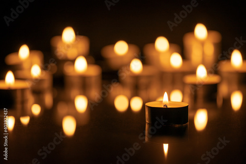 A FOCUSED LIGHTED CANDLE AND MANY OTHERS DEFOCUSED AT THE BACK. ALL SOULS DAY CONCEPT. DARK BACKGROUND. photo