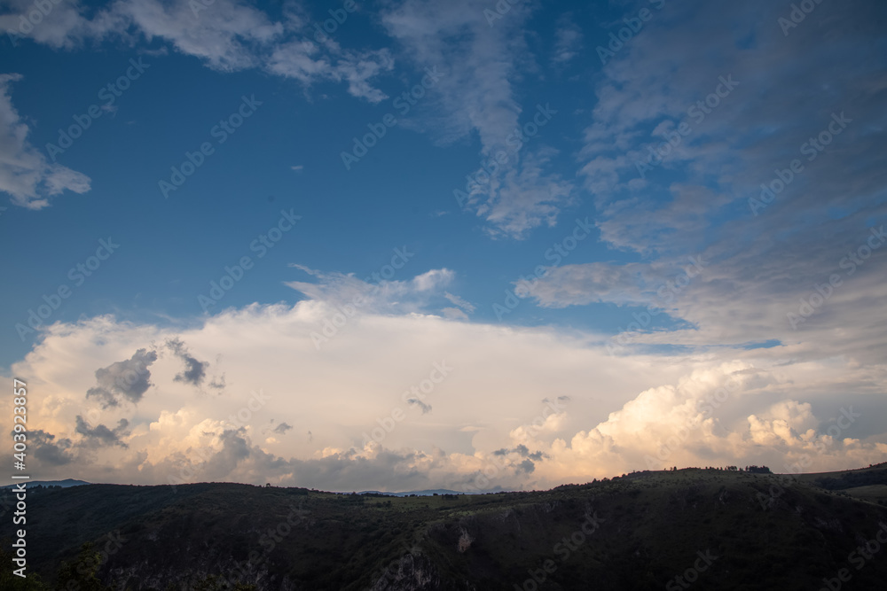 Scenic canyon view of meanders on the river Uvac, on the Zlatar Mountain with beautiful sunset with dramatic and fluffy white clouds and sky in background. Uvac is a special nature reserve in Serbia.