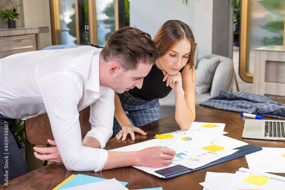 Two adult Caucasian men and women business people having discussion and brainstorm an idea while writing note on document and paper on working table inside of office work space. Teamwork concept. Two adult Caucasian men and women business people having discussion and brainstorm an idea while writing note on document and paper on working table inside of office work space. Teamwork concept.