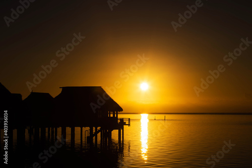 Sun rises over tropical island ocean with vacation destination overwater bungalows