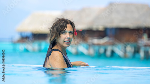 Pretty woman swims in blue infinity pool at a tropical island resort during vacation