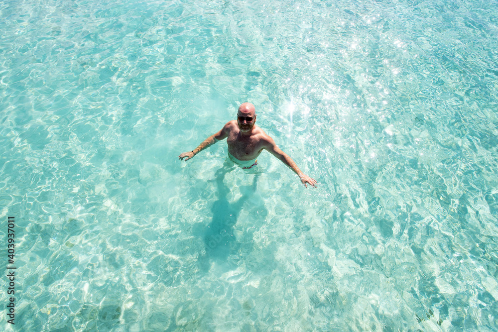 Bald man swimming in clear turquoise tropical island ocean water