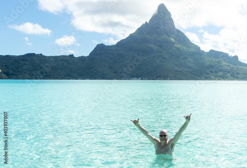 Bald man with his arms raised in a Bora Bora tropical island turquoise ocean water lagoon with Mt. Otemanu in the background © Mat Hayward