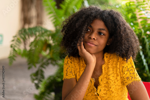 Young black woman with curly hair, yellow dress and black hat, sitting in restaurant waiting