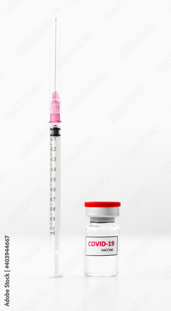 Clear vial with a red cap with the word covid-19 affixed to the side of the vial. Next to it is a syringe. Placed on the table White background copy space concept virus medicine, covid-19 Clear vial with a red cap with the word covid-19 affixed to the side of the vial. Next to it is a syringe. Placed on the table White background copy space concept virus medicine, covid-19