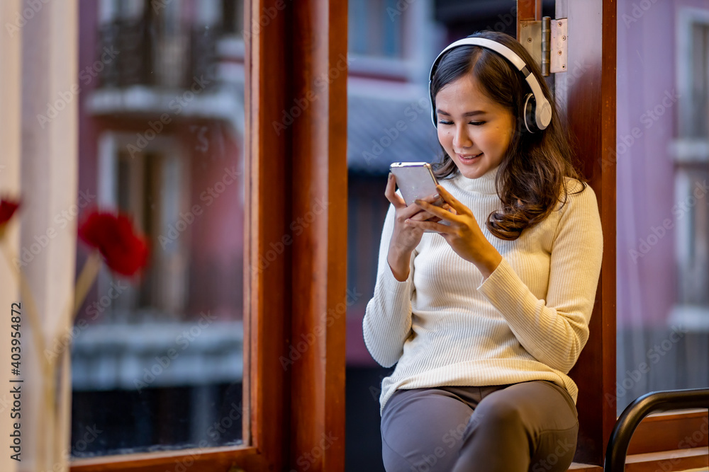 Beautiful woman with headphone sitting at the window sill while use mobile phone. Beautiful woman with headphone sitting at the window sill while use mobile phone.