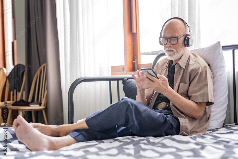 Old man with white beard take a rest in the room while listening music by headphone.
