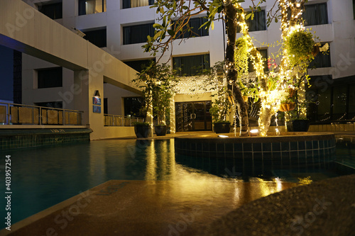 Night pool with beautiful lighting and wood. Romantic mood in hotels. The water reflects the light of the lights that are located on the tree in the middle of the pool and at the entrance. Thailand