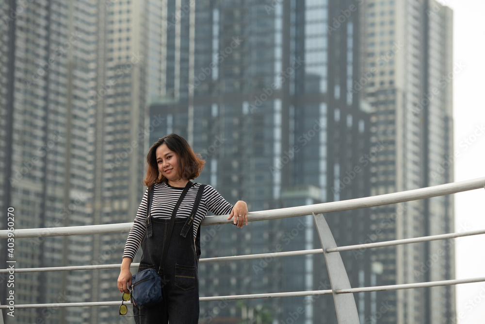 Happy Asian Female standing outdoors smiling with city and building in the background 