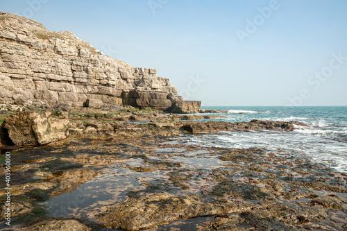 Tidal pools on rocky beach beside rocky cliff face with blue sky