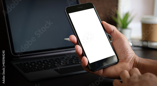 Close up view of man hand holding mock up smart with blank screen at his modern workspace.Blank screen for graphics display montage.