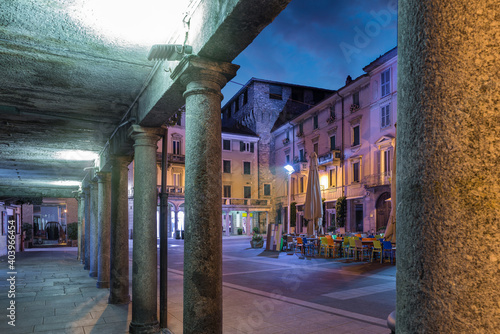 Downtown deserted city street scene at night. Lecco, Italy. Picturesque town overlooking lake Como. Square XX Settembre and the old Viscontea tower seen from the arcades