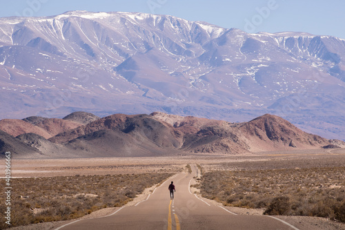 Hombre caminando por la carretera hacia una enorme montaña nevada