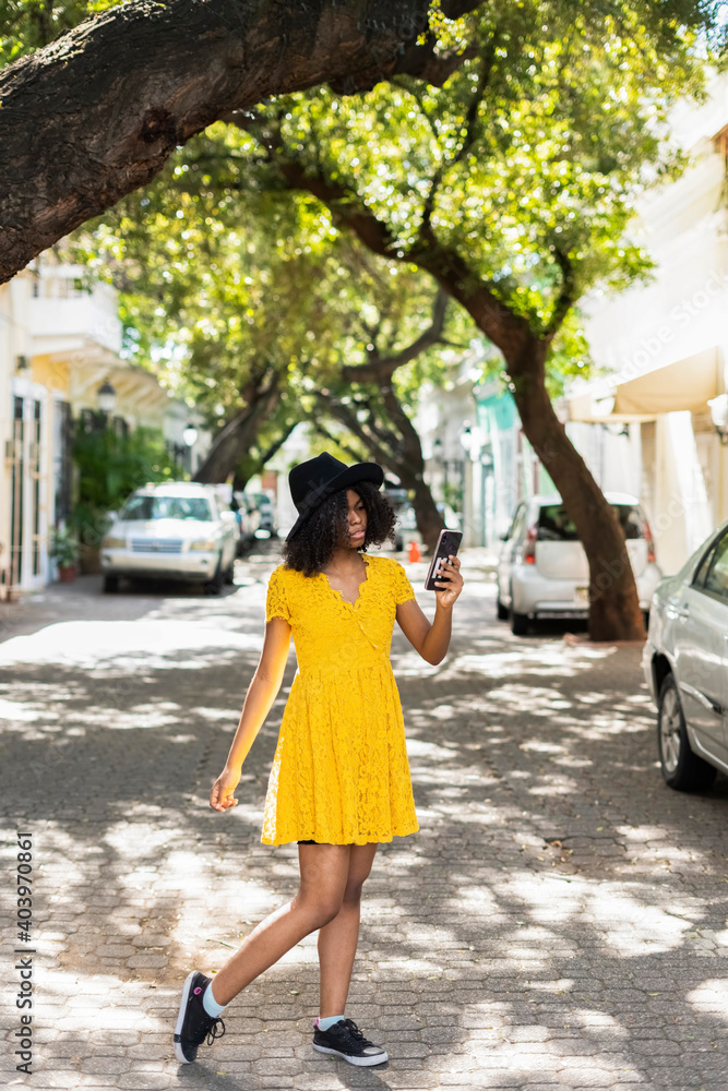 young black woman with curly hair, with red mask, yellow dress, using her smart phone