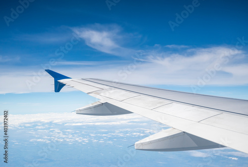 Aircraft Wing on beautiful blue sky and cloud background in altitude during flight. Wing of an airplane looking from the window.