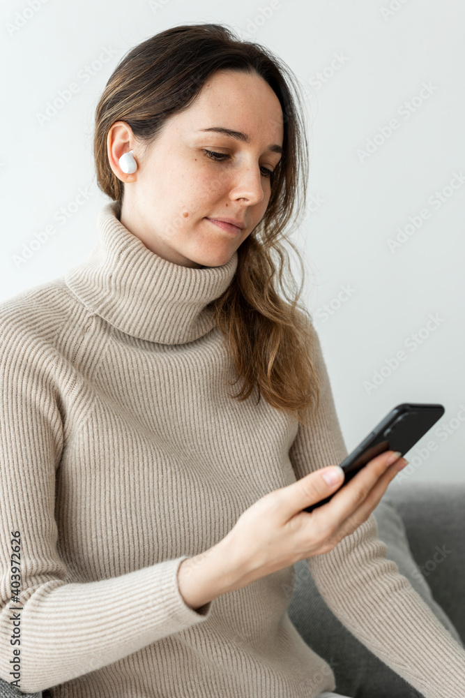 Woman wearing wireless earbuds and using a mobile phone Woman wearing wireless earbuds and using a mobile phone