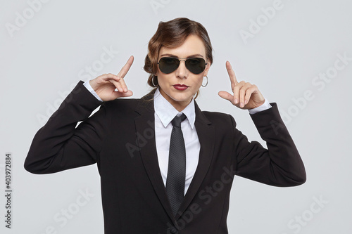 attractive woman with a retro hairstyle poses in a men's suit and sunglasses