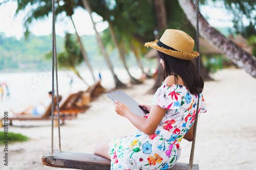 Young girl sitting on swing on the beach using digital tablet