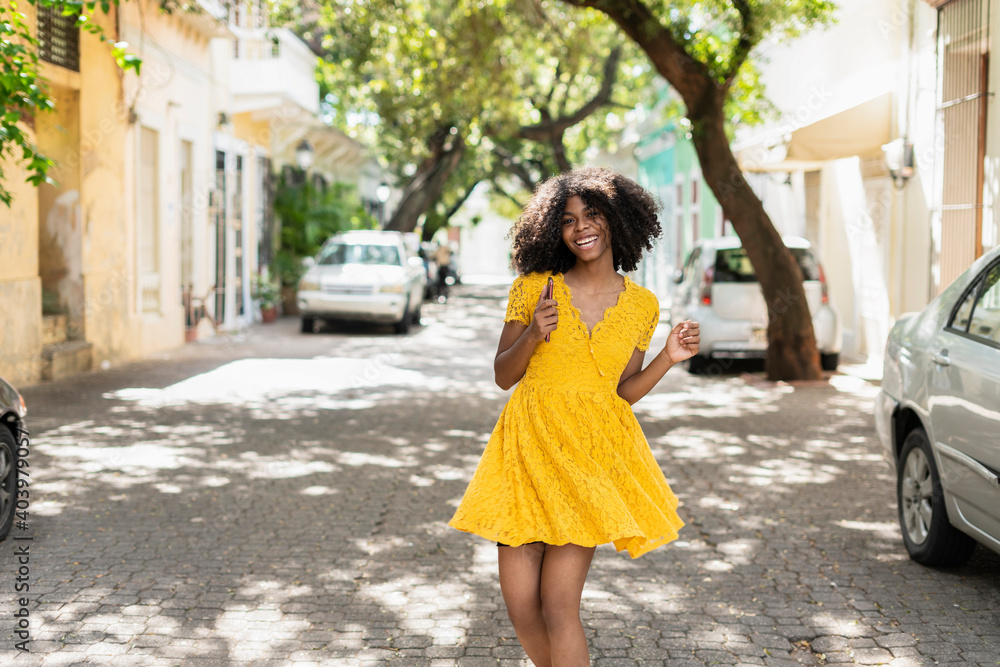 Naklejka premium Young black woman with curly hair, in yellow dress and with styles, attitude, laughing, happy