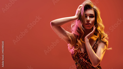 Portrait of beautiful young woman with bright shiny makeup. Blonde with brightly colored long hair. Pretty girl with long curly hair.   Fashion model in a shiny dress posing at studio. © Valua Vitaly