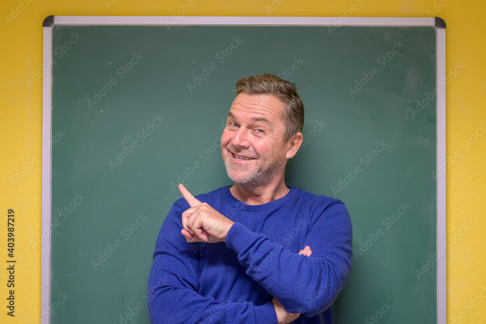 Male teacher pointing to the chalkboard behind him