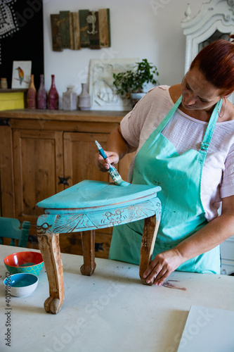 Fotografia Mature craftswoman painting and restoring antique furniture in carpentry worksho