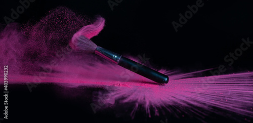 Pink makeup powder brush fall on shiny black surface in a dust cloud