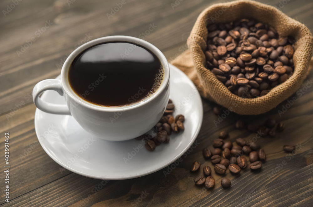 Cup of coffee with burlap sack of roasted beans on wooden table Cup of coffee with burlap sack of roasted beans on wooden table