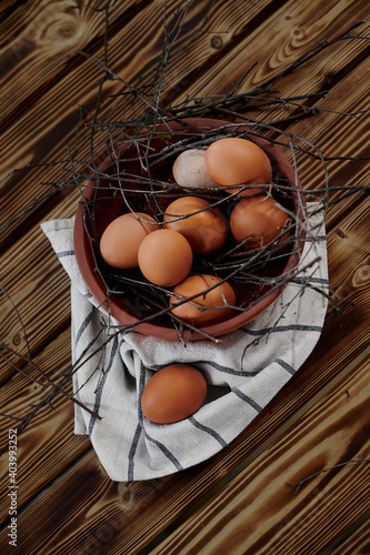 chicken eggs in brown bowl with branches on wooden table and cloth with stripes