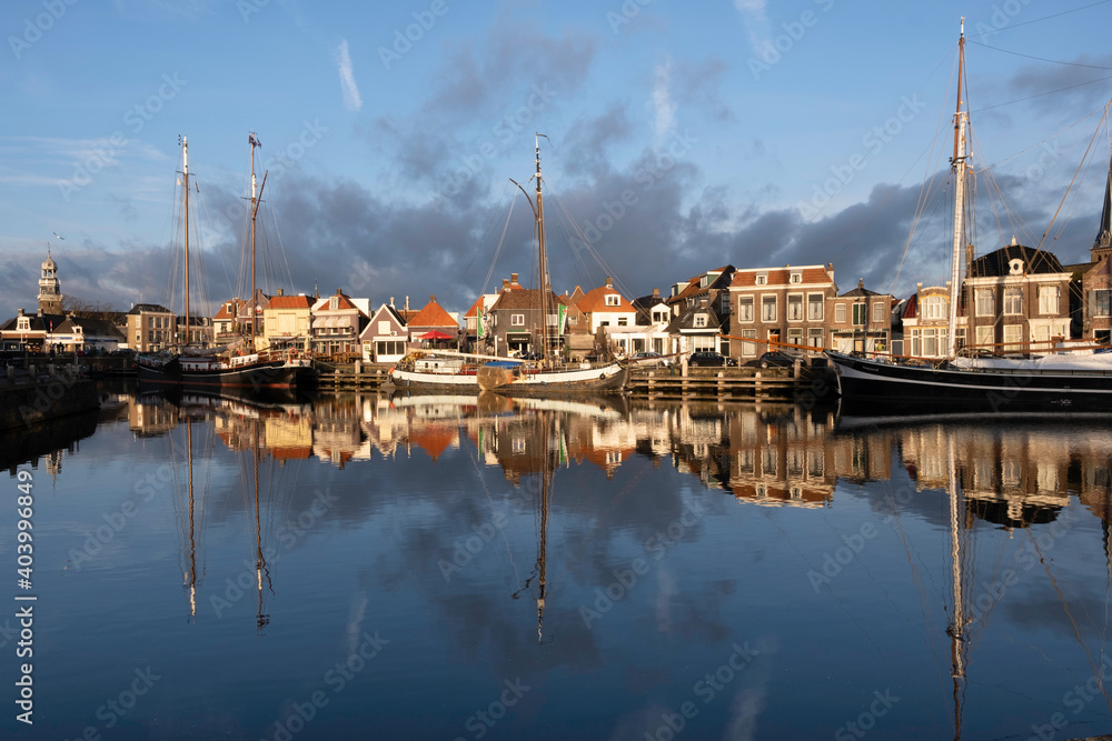 Large sail boats and pleasure yachts mirrored in blue water with sunset in the port of Lemmer in Friesland, Netherlands