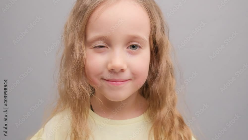 Little girl looks at the camera and laughs. Portrait of a child in the studio on a gray background close-up. Super slow motion. Little girl looks at the camera and laughs. Portrait of a child in the studio on a gray background close-up. Super slow motion.