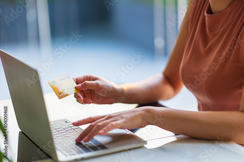 Woman's hands holding a  mock up credit card and using laptop for online shopping.