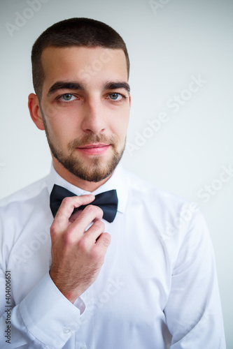 Young male businessman dressed in a white shirt with a short beard wears a black bow tie