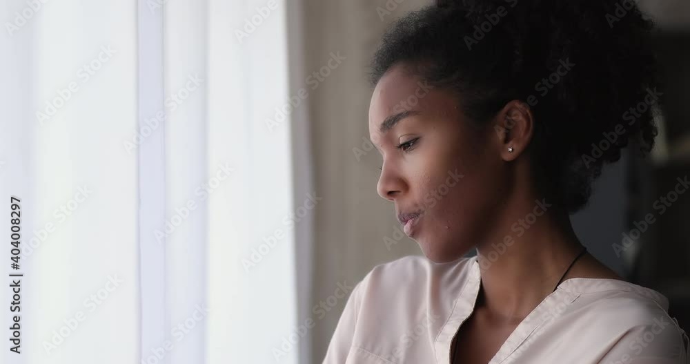 Young african woman standing indoor looking out window thinking, lost in sad thoughts having personal life or health concerns feels upset. Break up, divorce, psychological disorder, loneliness concept Young african woman standing indoor looking out window thinking, lost in sad thoughts having personal life or health concerns feels upset. Break up, divorce, psychological disorder, loneliness concept