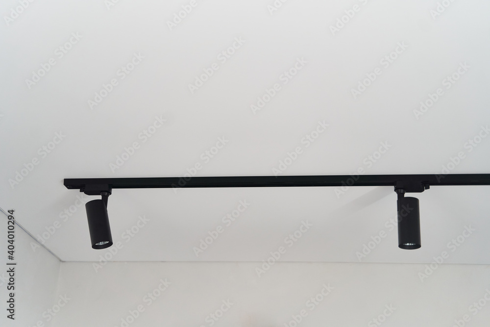 Modern LED black track spot lights in the interior. Hanging lamps spotlights attached to a concrete ceiling in an office loft room Modern LED black track spot lights in the interior. Hanging lamps spotlights attached to a concrete ceiling in an office loft room
