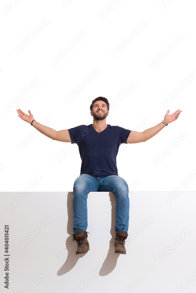 Happy Handsome Man Is Sitting On A Top With Arms Outstretched, Looking Up And Enjoying The View Happy Handsome Man Is Sitting On A Top With Arms Outstretched, Looking Up And Enjoying The View