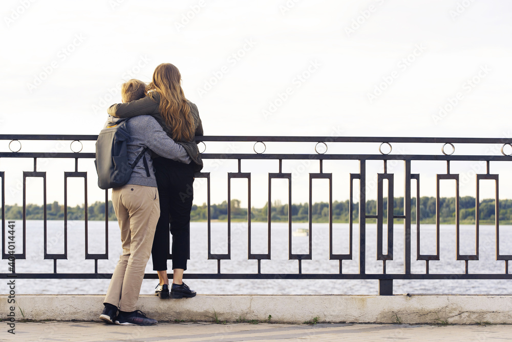 A loving couple stands in an embrace on the background of the embankment. View from the back. Unrecognizable faces