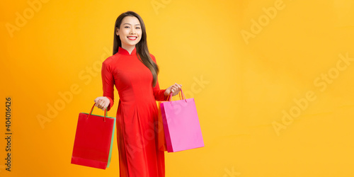 Cheerful young woman wearing ao dai dress hold shopping bags