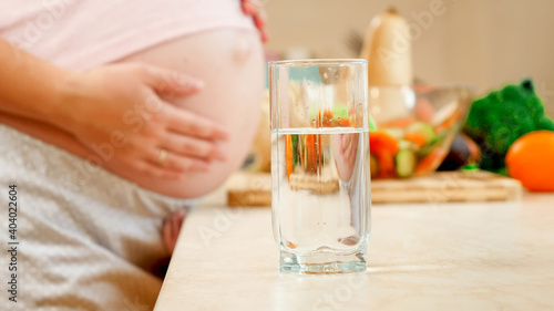 Portrait of smiling pregnant woman touching her big belly and drinking water. Concept of healthy lifestyle, nutrition and hydration during pregnancy