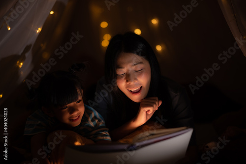 young Asian mother read the story in the book for her daughter children on the bed at home, family and motherhood learning concept © chokniti