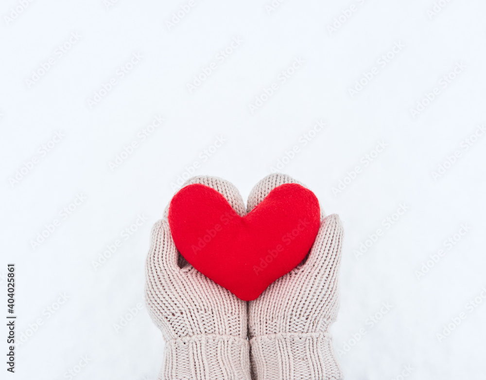 Creative greeting card for Valentines Day. Hold red soft heart toy made of fabric in beige mittens against background of white freshly fallen snow. Empty space for your greeting text. Creative greeting card for Valentines Day. Hold red soft heart toy made of fabric in beige mittens against background of white freshly fallen snow. Empty space for your greeting text.