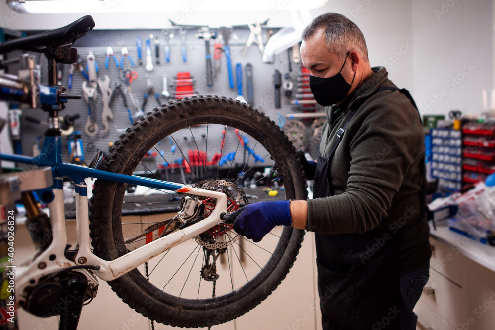 mechanic fixing blue and white mountain bike wheel next to tool bench with mask mechanic fixing blue and white mountain bike wheel next to tool bench with mask