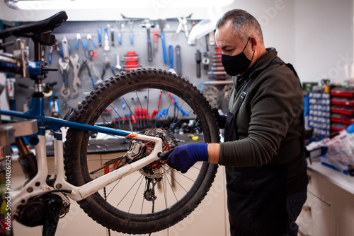 mechanic fixing blue and white mountain bike wheel next to tool bench with mask