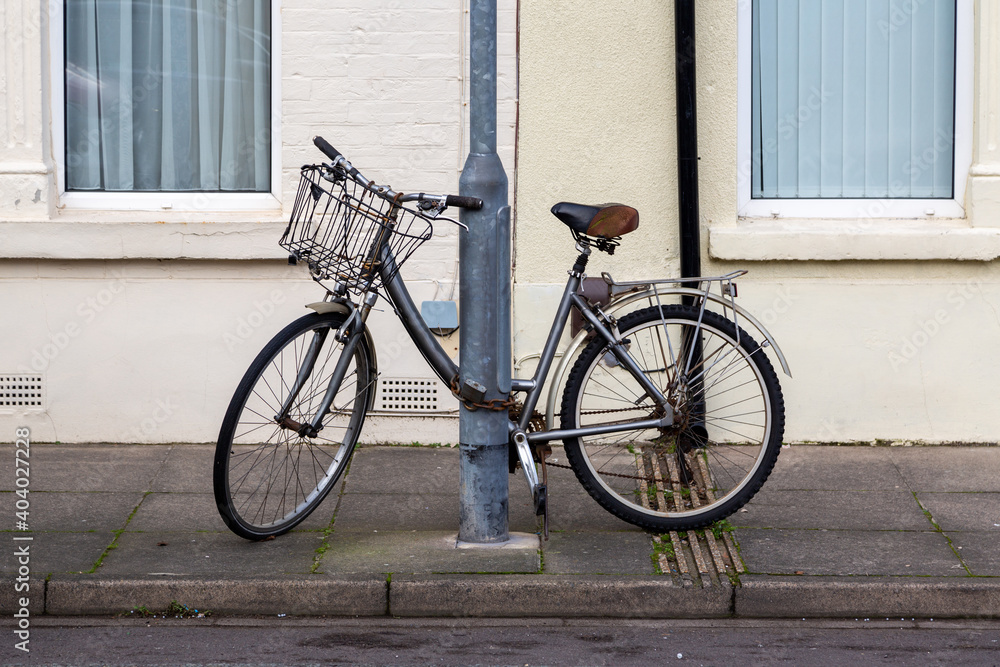 An old ladies bike with a basket chained to a lamppost in the street An old ladies bike with a basket chained to a lamppost in the street