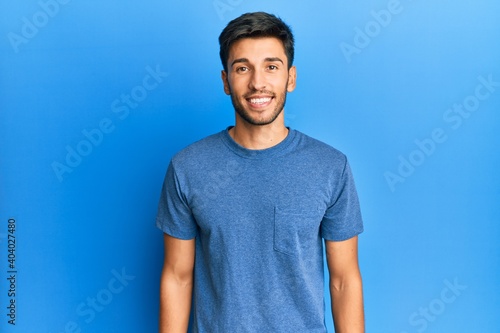 Young handsome man wearing casual tshirt over blue background with a happy and cool smile on face. lucky person.