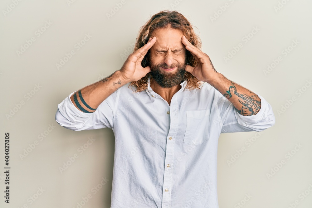 Handsome man with beard and long hair wearing casual white shirt with hand on head, headache because stress. suffering migraine. Handsome man with beard and long hair wearing casual white shirt with hand on head, headache because stress. suffering migraine.