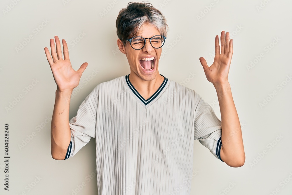Young hispanic man wearing casual clothes and glasses celebrating mad and crazy for success with arms raised and closed eyes screaming excited. winner concept Young hispanic man wearing casual clothes and glasses celebrating mad and crazy for success with arms raised and closed eyes screaming excited. winner concept