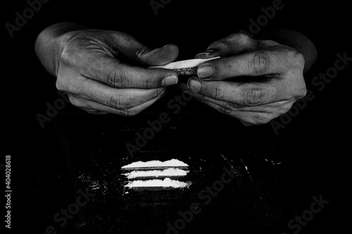 Drug addict man is preparing to snorting cocaine powder with rolled dollar banknote. Narcotics concept. Monochrome, black and white photo. Close-up macro shot. High resolution sharp photo.